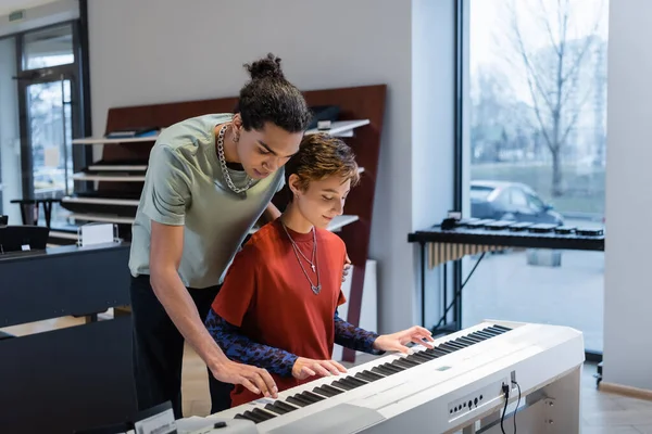 Young woman playing synthesizer with african american boyfriend in music store — Foto stock