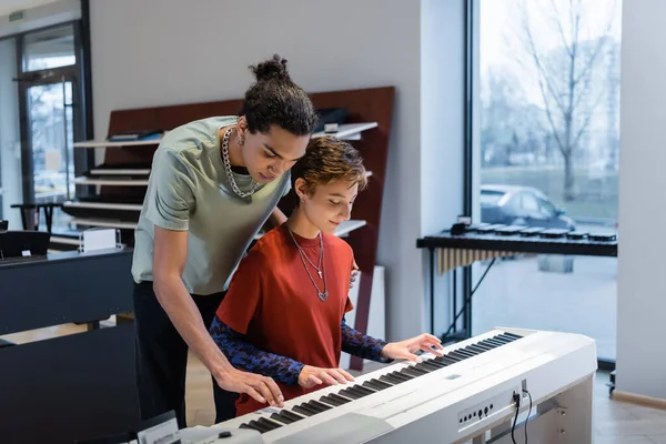 Junge Frau spielt Synthesizer mit afrikanisch-amerikanischem Freund in Musikladen — Stockfoto