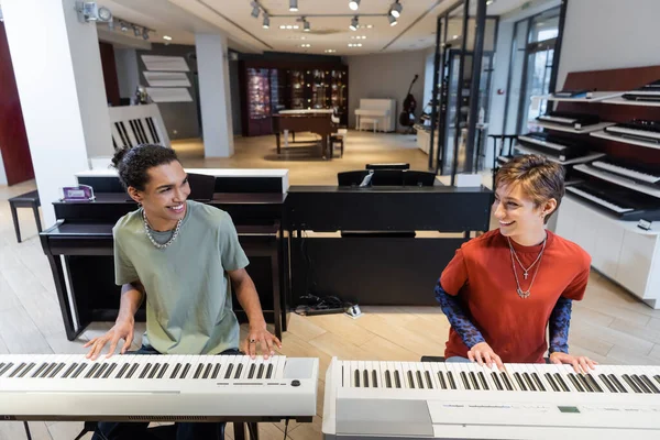 Positive multiethnic couple playing synthesizers in music shop — Fotografia de Stock