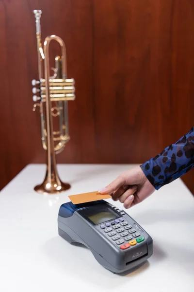 Cropped view of woman paying with credit card near blurred trumpet in music store - foto de stock