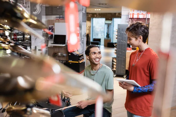 Seller holding digital tablet near african american man playing electric drums in store — Stock Photo