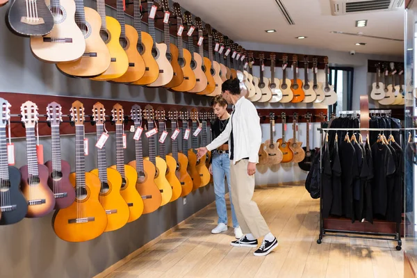 Vendedor afroamericano tocando guitarra acústica cerca de comprador en tienda de música - foto de stock