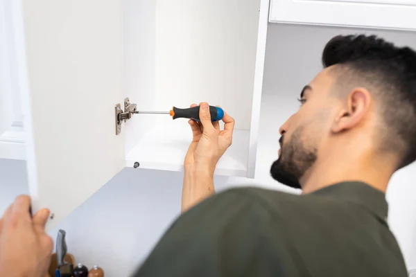 Side view of blurred arabian craftsman with screwdriver fixing cabinet in kitchen — Stock Photo