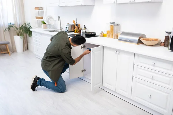Young arabian craftsman fixing cabinet under worktop in kitchen — Photo de stock
