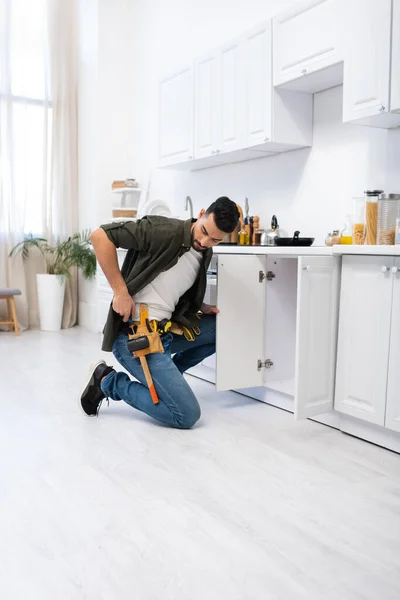 Arabian man looking at tool belt near cabinet in kitchen — Stock Photo