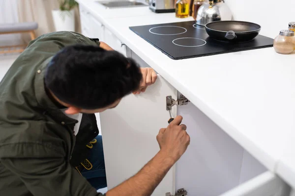 Blurred craftsman with screwdriver fixing metal hinge in kitchen cabinet — Stock Photo