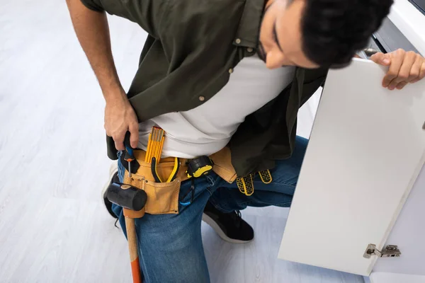 High angle view of arabian man taking screwdriver from tool belt near kitchen cabinet — Stock Photo