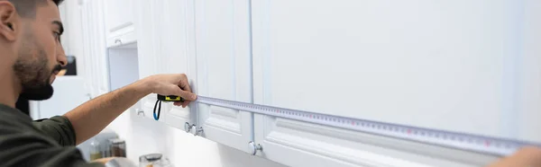 Side view of arabian man measuring cupboards in kitchen at home, banner - foto de stock