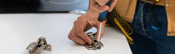 Cropped view of man with tool belt fixing hinge of cupboard, banner - foto de stock