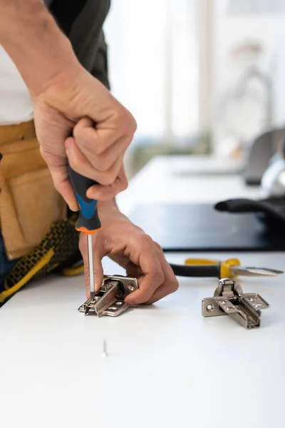 Cropped view of man with screwdriver fixing hinge of cupboard - foto de stock