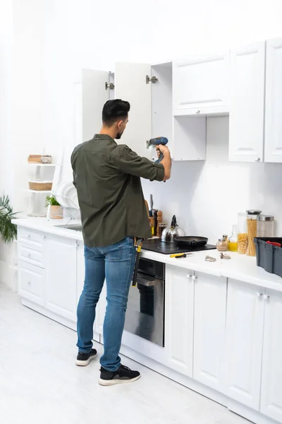 Muslim man using electric screwdriver while fixing kitchen cupboard — Fotografia de Stock