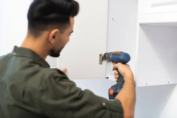 Blurred arabian man with electric screwdriver fixing hinge in kitchen cupboard — Stockfoto