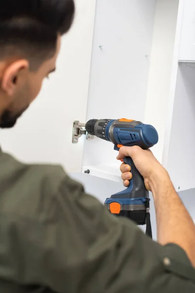 Blurred muslim man fixing door of cupboard with electric screwdriver at home — Stock Photo