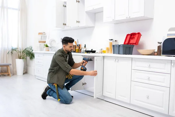 Молодий арабський чоловік з викруткою, що фіксує двері кухонного шафи — стокове фото