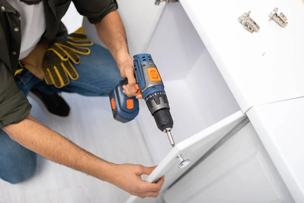 Top view of craftsman with electric screwdriver fixing kitchen cabinet — Photo de stock