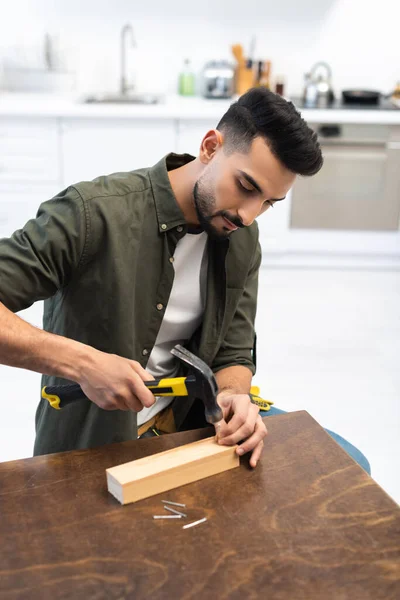 Arabian man holding hammer and nail near wooden board at home — Stockfoto