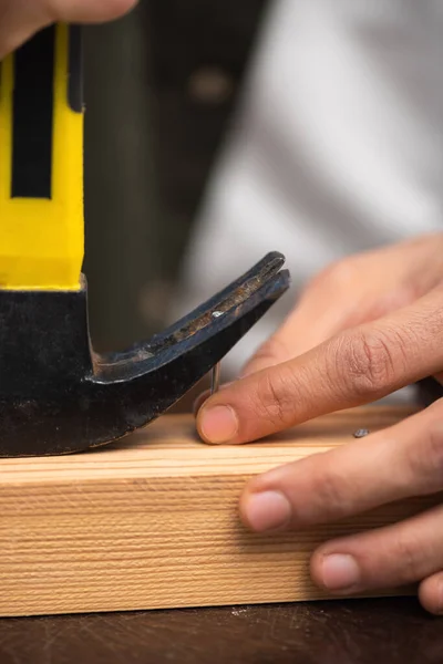 Cropped view of man picking up nail with manner near wooden board — Photo de stock