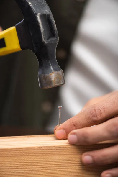 Cropped view of man holding nail on wooden plank and hammer at home — Fotografia de Stock