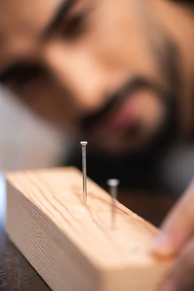 Blurred repairman looking at nails in wooden board — Stockfoto