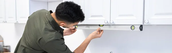 Arabian man measuring kitchen cupboard with spirit level at home, banner — Photo de stock