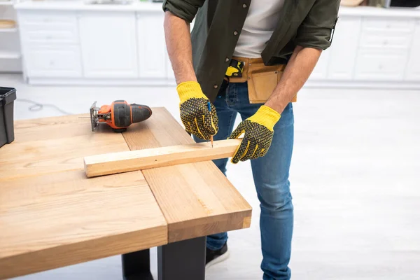 Cropped view of craftsman in gloves marking wooden plank at home — Stockfoto