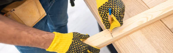 Cropped view of carpenter in gloves marking wooden board at home, banner — Foto stock