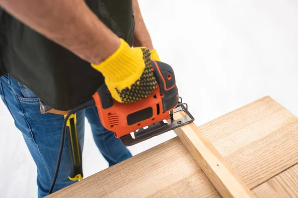 High angle view of man holding electric jigsaw machine near wooden plank at home - foto de stock
