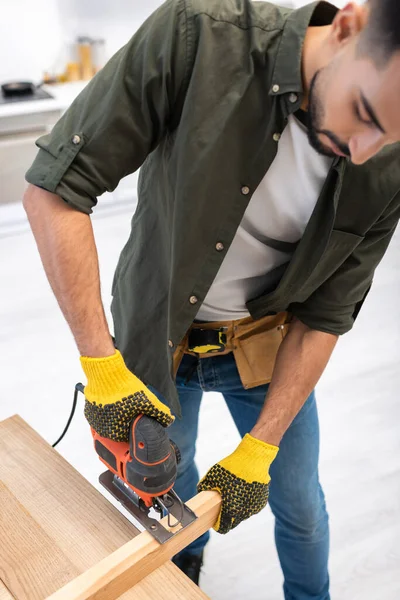 High angle view of young muslim carpenter holding jigsaw machine near wooden board at home — Stock Photo