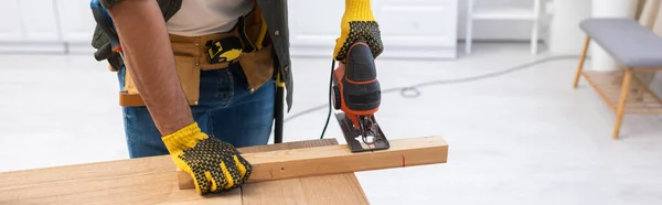 Cropped view of carpenter in tool belt sawing wooden plank at home, banner — Photo de stock