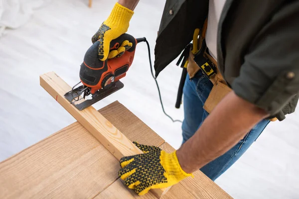 High angle view of carpenter in gloves sawing wooden board on table at home — Photo de stock