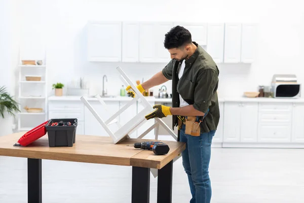 Arabian man with tool belt holding chair on table at home — Foto stock