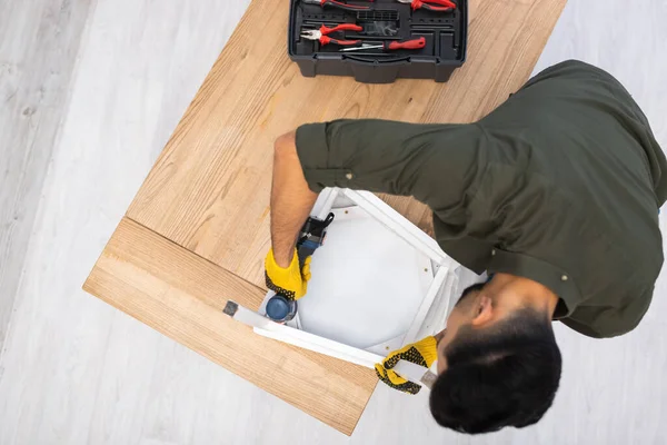 Overhead view of muslim craftsman fixing chair with electric screwdriver on table at home - foto de stock