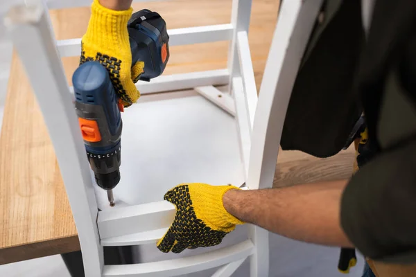 Cropped view of man in gloves fixing chair with electric drill at home — Fotografia de Stock