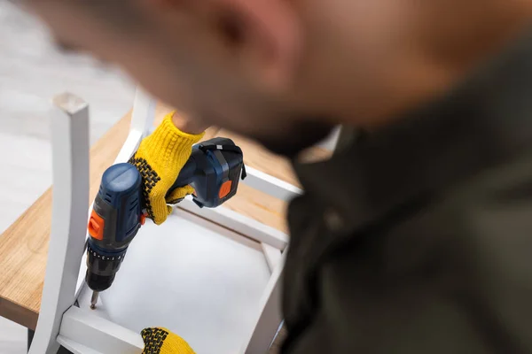 Blurred man in protective gloves fixing chair with electric drill at home — Fotografia de Stock