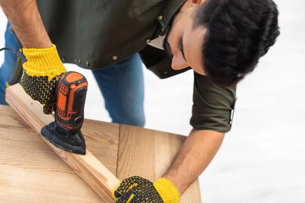 Arabian carpenter sanding wooden board with electric sander at home — Fotografia de Stock