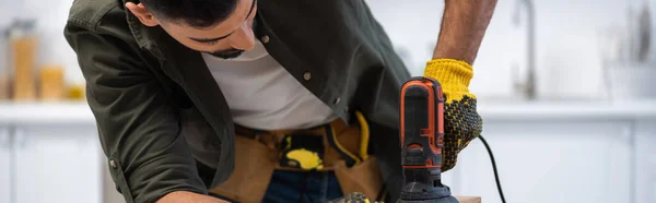 Young arabian man in glove and tool belt holding sander at home, banner — Fotografia de Stock