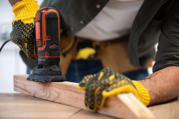 Cropped view of carpenter sanding wooden plank with tool at home — Stockfoto