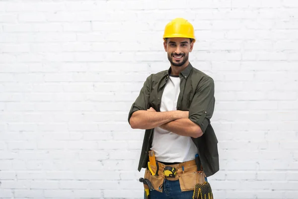 Cheerful arabian repairman in hardhat crossing arms at home — Foto stock