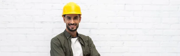 Позитивний арабський ремонтник у шоломі, дивлячись на камеру вдома, банер — стокове фото