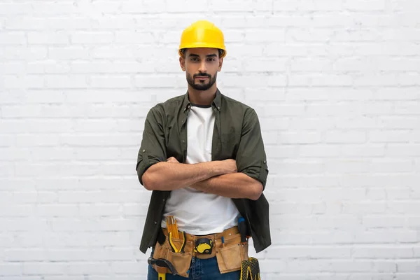 Young muslim handyman in helmet and tool belt looking at camera at home — Fotografia de Stock