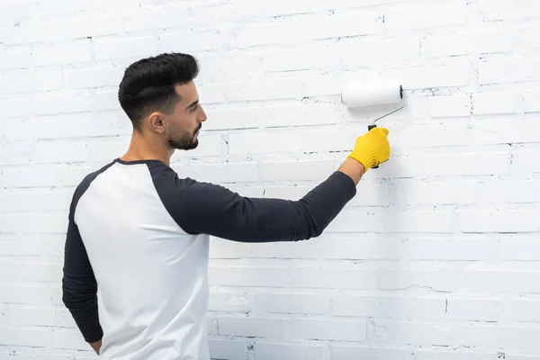 Side view of muslim man in glove coloring brick wall at home — Fotografia de Stock