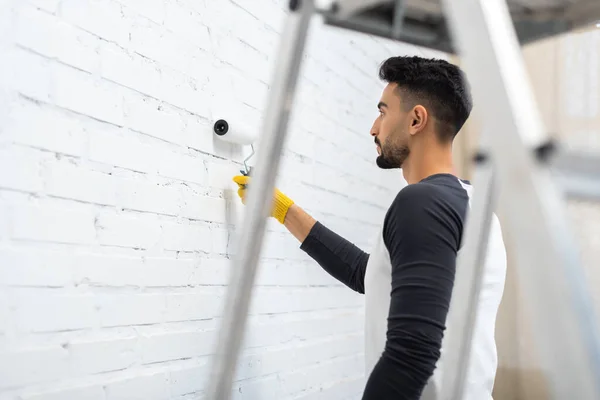 Side view of arabian man coloring brick wall near blurred ladder at home — Photo de stock