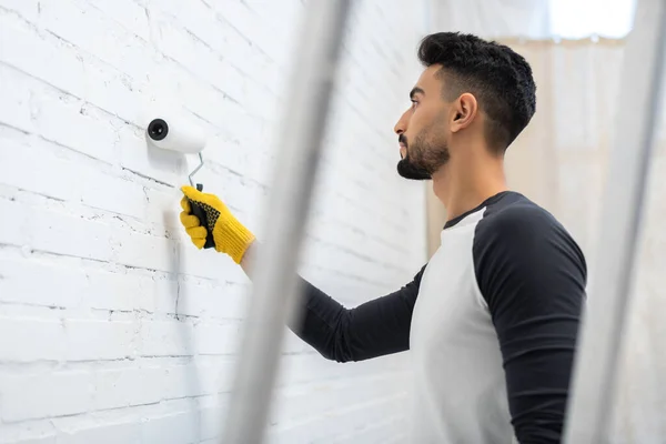 Side view of muslim man painting white brick wall at home — Stock Photo