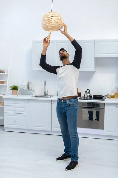 Arabian man holding lightbulb near chandelier in kitchen — Stock Photo