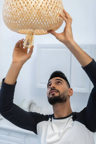 Muslim man holding lightbulb near chandelier in kitchen — Stockfoto