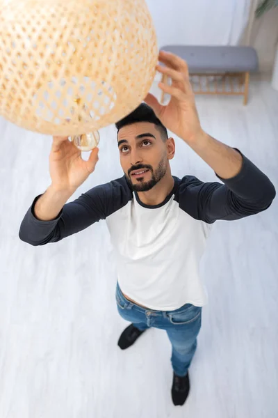 High angle view of smiling muslim man changing lightbulb in chandelier at home — Photo de stock