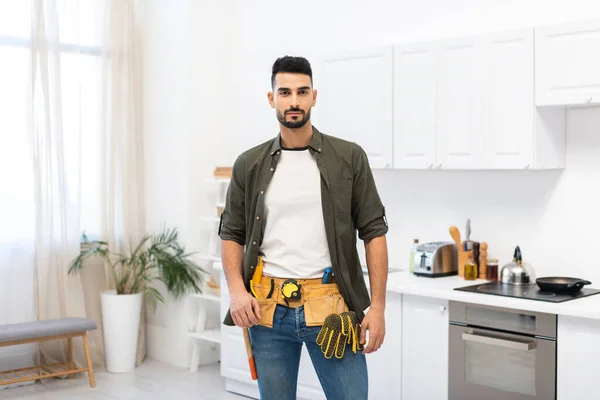 Аравійський чоловік у панцирі інструментів дивиться на камеру на кухні. — стокове фото
