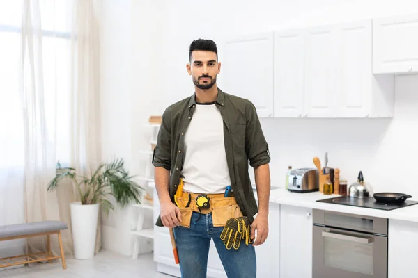 Arabian man in tool belt looking at camera in kitchen — Stock Photo