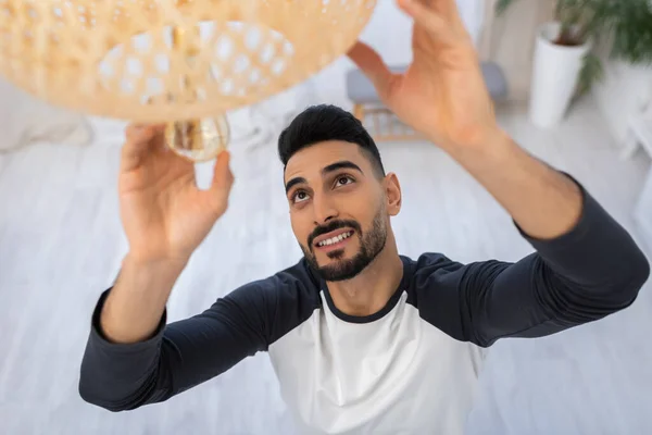 High angle view of smiling arabian man changing lightbulb at home - foto de stock