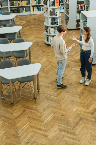 High angle view of teenage students gesturing during conversation in library - foto de stock